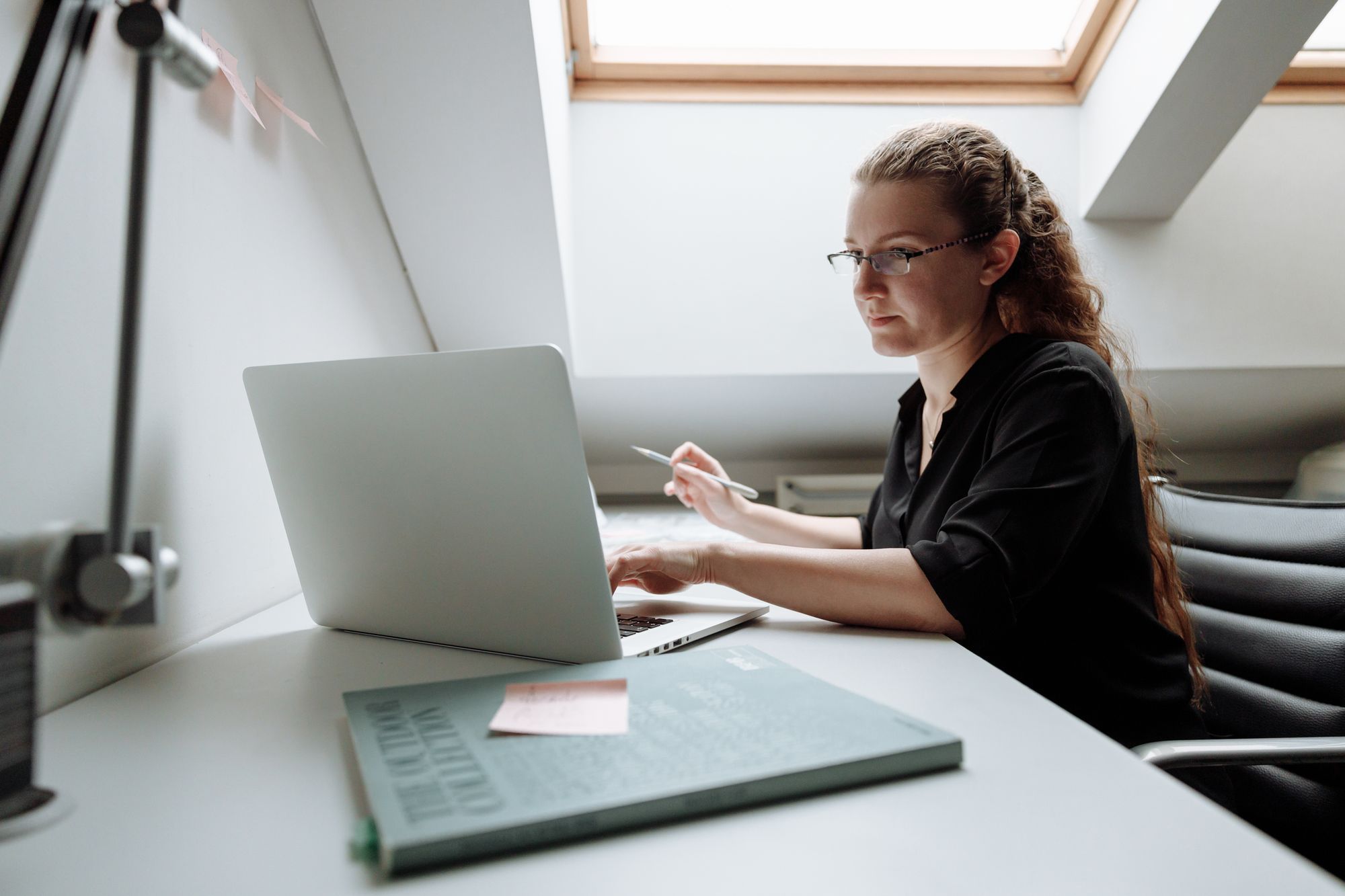 Eine Frau arbeitet an einem hellen Schreibtisch unter der Dachschräge am Laptop.